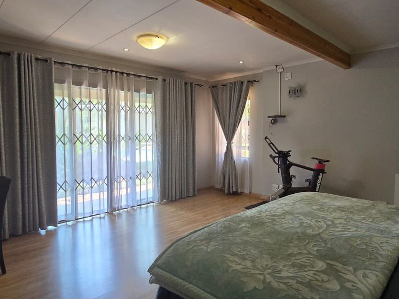 Spacious bedroom featuring laminate flooring, an exposed timber ceiling beam, and a sliding glass door with security gate providing access to the outdoors.