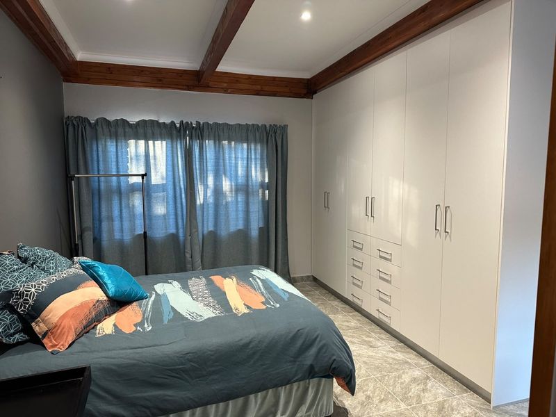 A well-maintained bedroom featuring modern built-in cupboards, tiled flooring, and distinctive exposed timber ceiling beams.