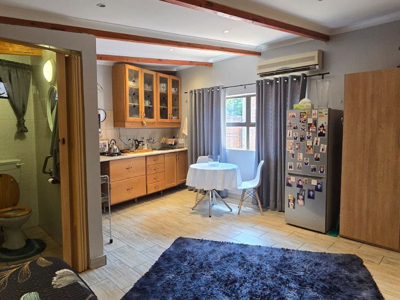 Open-plan living area featuring tiled floors, exposed timber ceiling beams, built-in cabinetry, and an adjoining en-suite bathroom.