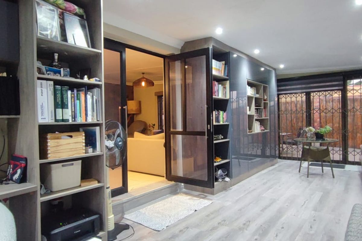 A modern living area featuring laminate flooring, recessed lighting, and extensive built-in cabinetry, with direct access to an outdoor patio through sliding glass doors.