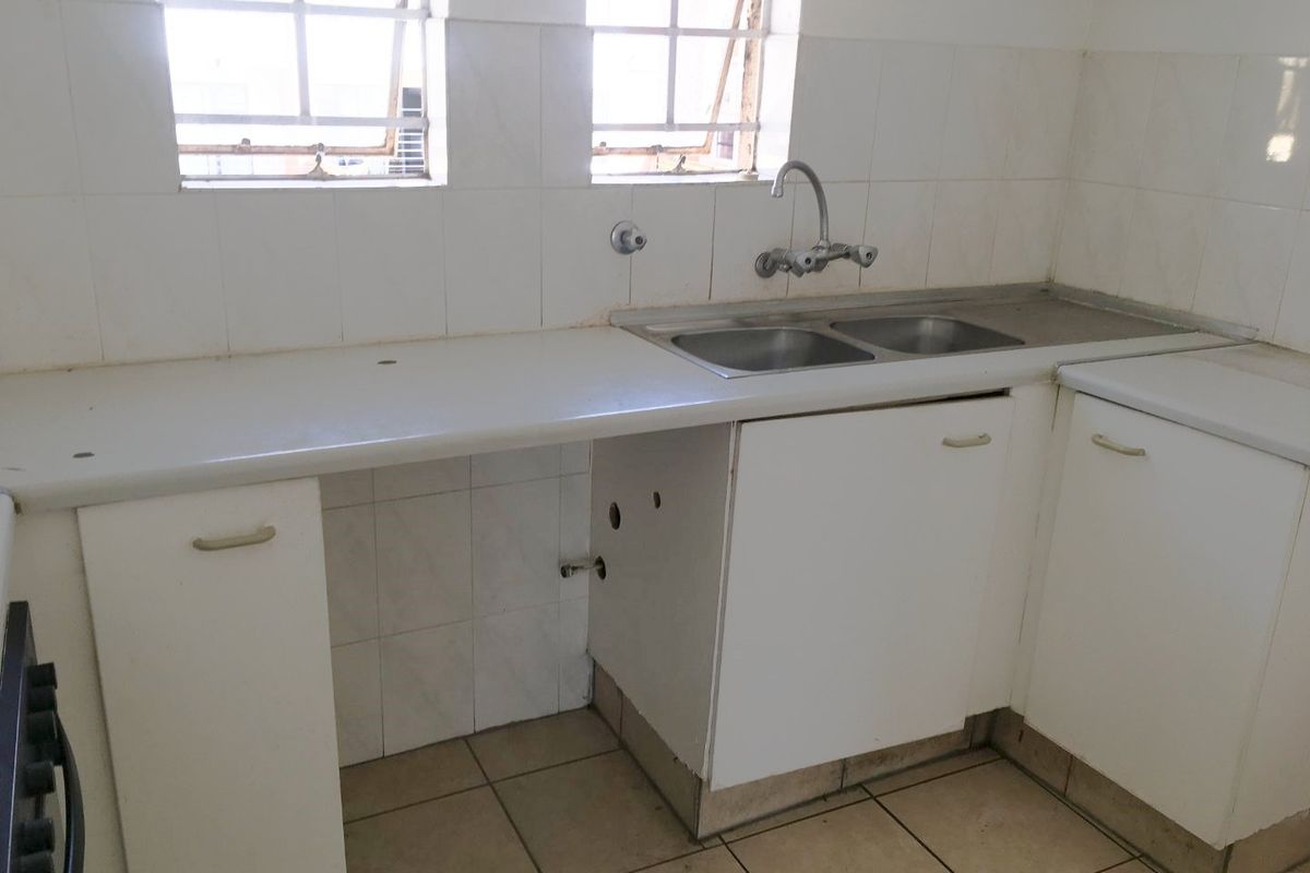 A functional kitchen area featuring a double bowl sink, tiled splashback, and built-in cabinetry, ready for modernization and updates.