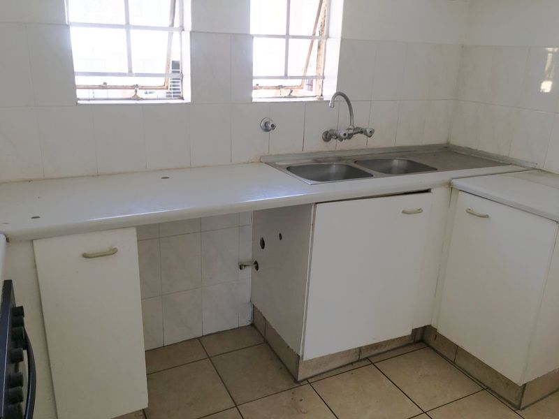 A functional kitchen area featuring a double bowl sink, tiled splashback, and built-in cabinetry, ready for modernization and updates.