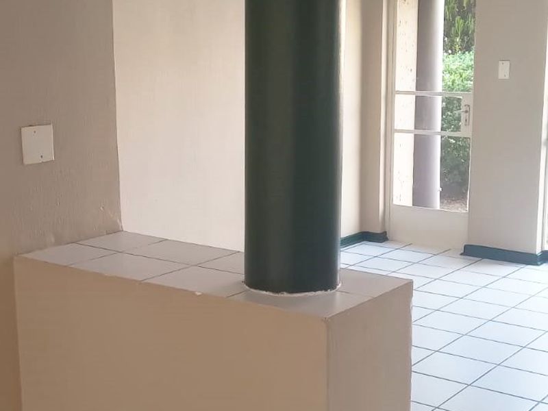 An empty open-plan living area featuring tiled flooring, a central structural column, and a glass-panelled door leading to the exterior.