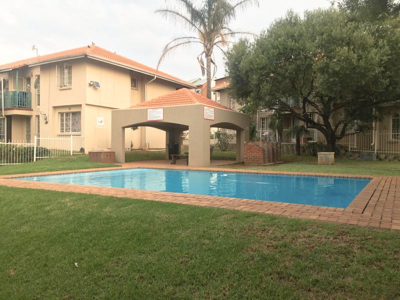 Communal swimming pool area featuring a covered gazebo, brick braai facility, and well-maintained lawn within the apartment complex grounds.