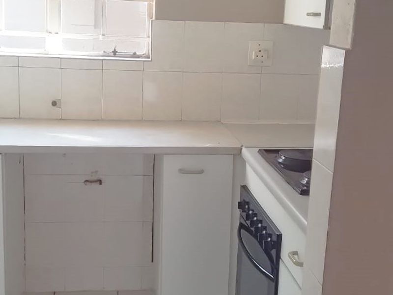 A compact kitchen featuring built-in cabinetry, a stove with oven, tiled flooring, and a tiled backsplash, offering a functional space ready for modernization.
