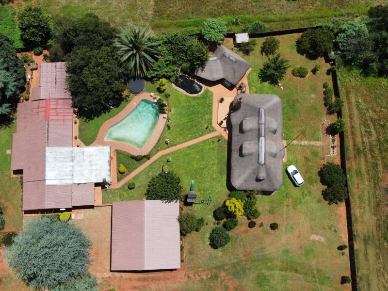 Aerial view of a farm property featuring multiple buildings with thatched and metal roofs, a swimming pool, and expansive garden grounds.