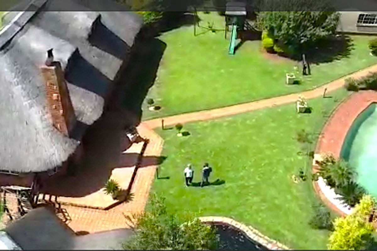 Aerial view of a farm property featuring a thatched roof house, a swimming pool, and landscaped garden areas with brick pathways.