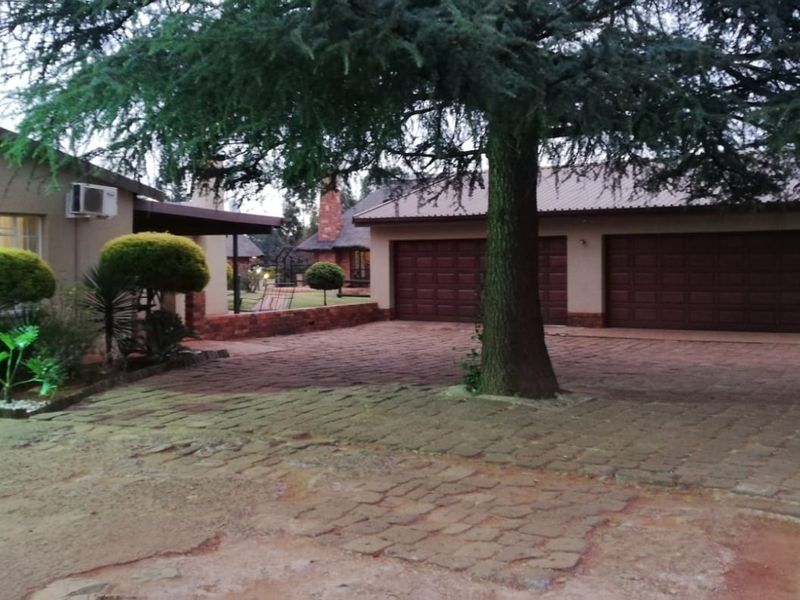 Front view of the farm property featuring a double garage, paved driveway, and established garden area with mature trees.