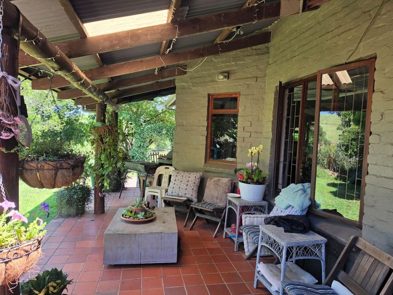 A covered patio area featuring tiled flooring, exposed timber beams, and brick walling, providing a rustic outdoor space overlooking the garden.