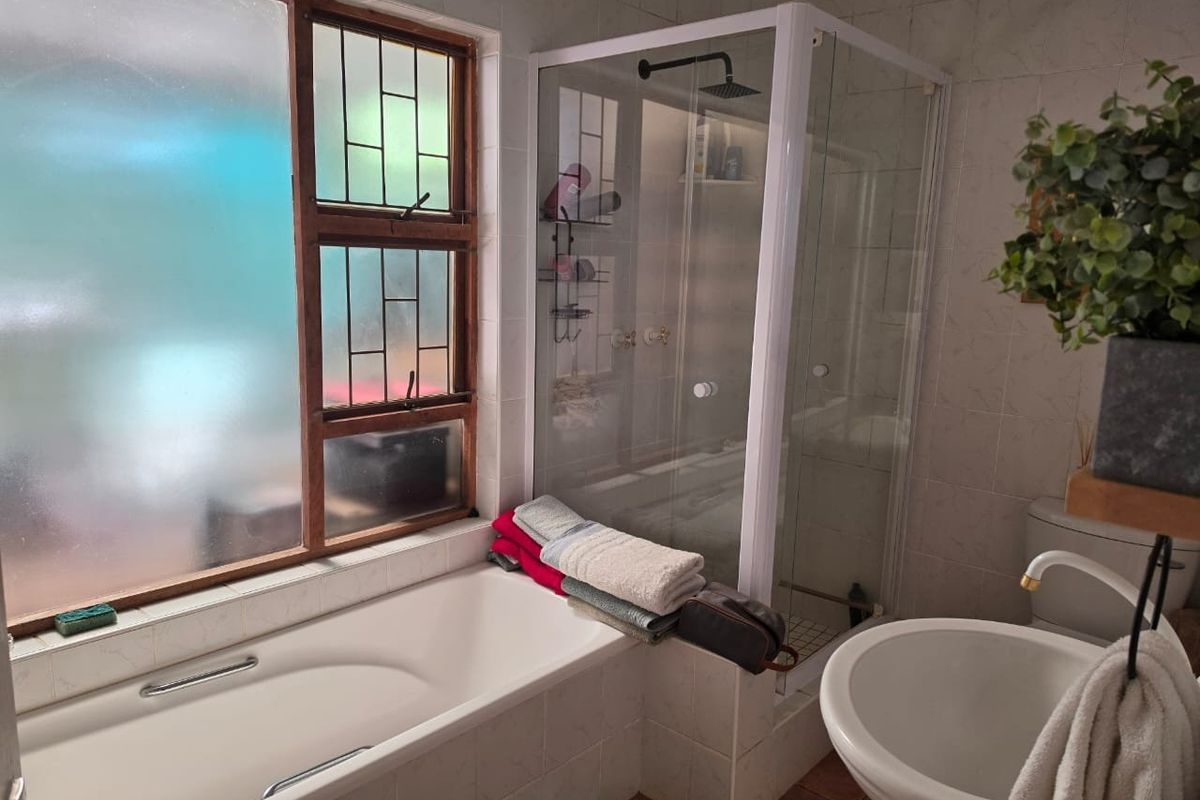 A functional bathroom featuring a built-in bathtub, a separate glass-enclosed shower with a rain shower head, a pedestal basin, and a toilet.