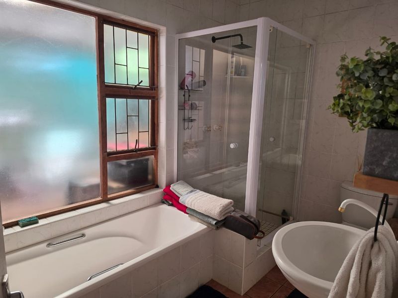 A functional bathroom featuring a built-in bathtub, a separate glass-enclosed shower with a rain shower head, a pedestal basin, and a toilet.