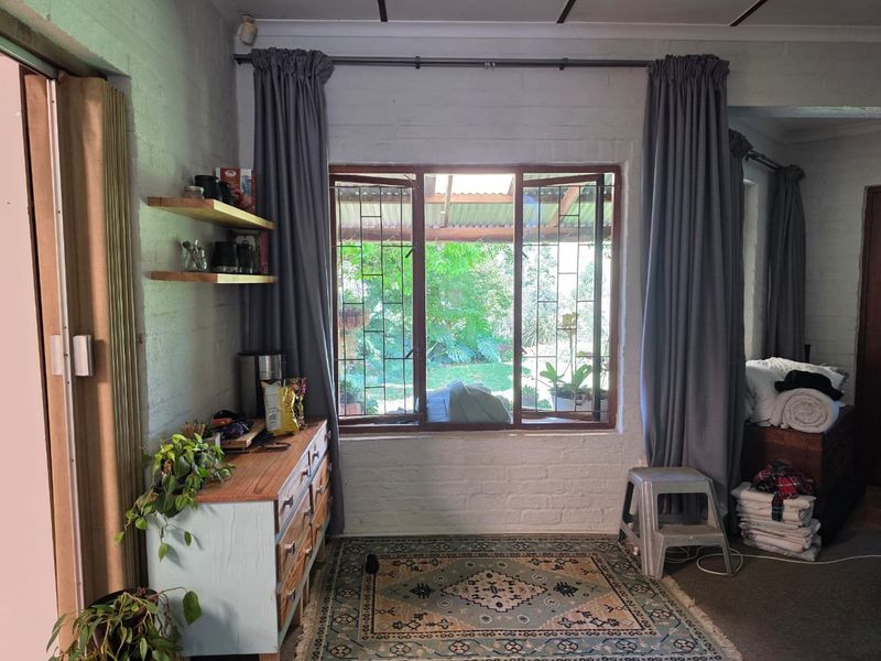 A living area featuring exposed brick walls, timber-framed windows with security bars, and floating timber shelving, offering a view into the garden.