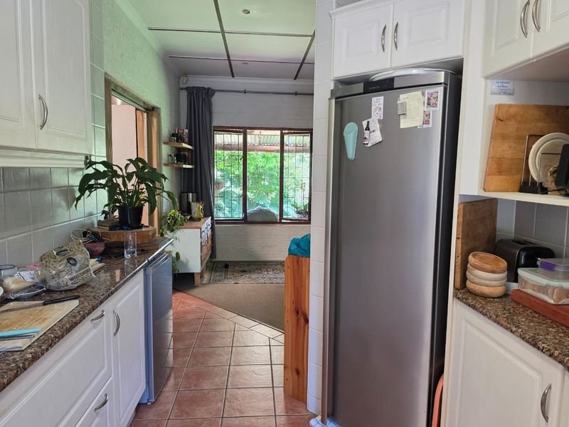 A functional kitchen featuring white cabinetry, granite countertops, and tiled flooring, leading into an adjacent living area with garden views.