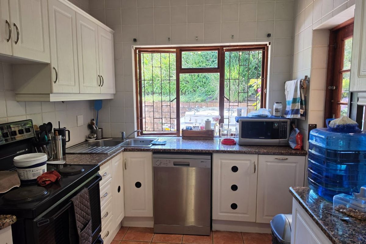 A functional kitchen featuring white cabinetry, granite countertops, tiled backsplash, and tiled flooring, with a window overlooking the garden area.