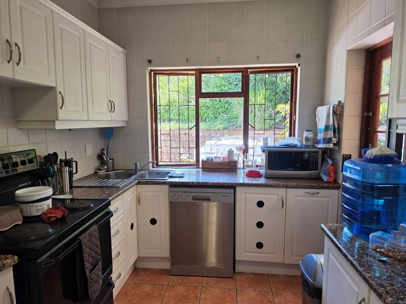 A functional kitchen featuring white cabinetry, granite countertops, tiled backsplash, and tiled flooring, with a window overlooking the garden area.