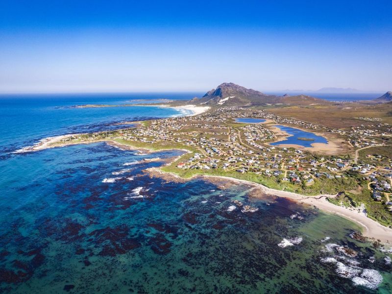 An expansive aerial view of the coastal residential area, showcasing the proximity to the ocean, natural landscape, and surrounding mountain scenery.