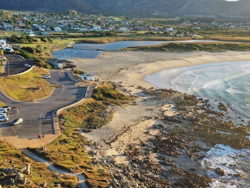 An aerial view of the coastal residential area, showcasing the beach, rocky shoreline, and adjacent paved parking facilities.