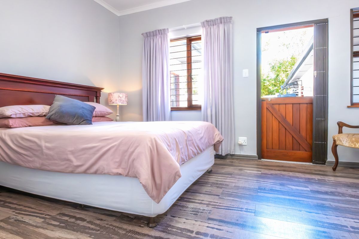 A well-maintained bedroom featuring laminate flooring, wooden window frames with security bars, and a stable-style wooden door providing direct access to the exterior.