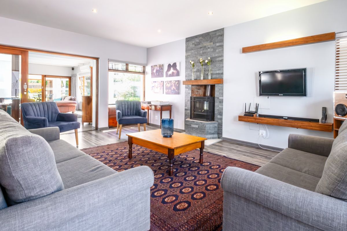 A bright and inviting living room featuring a stone-clad fireplace with a wood-burning stove, laminate flooring, and large sliding doors leading to an adjacent space.