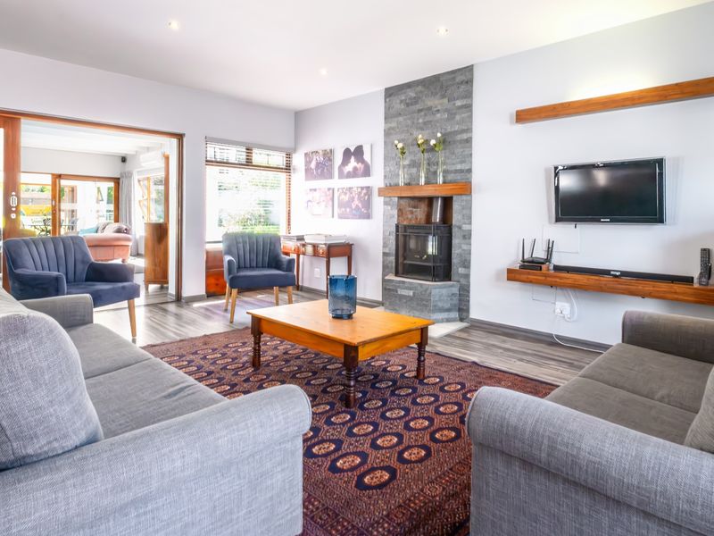 A bright and inviting living room featuring a stone-clad fireplace with a wood-burning stove, laminate flooring, and large sliding doors leading to an adjacent space.