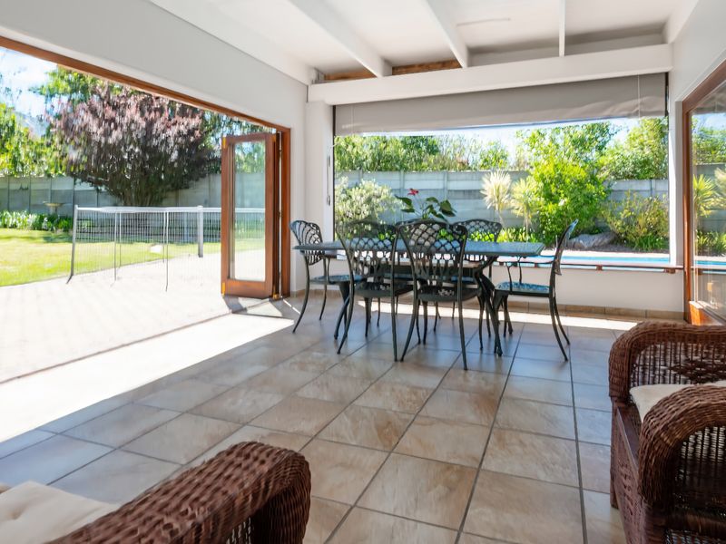 Spacious covered patio featuring tiled flooring and exposed beam ceiling, seamlessly connecting to the garden and pool area through large bi-fold and sliding doors.