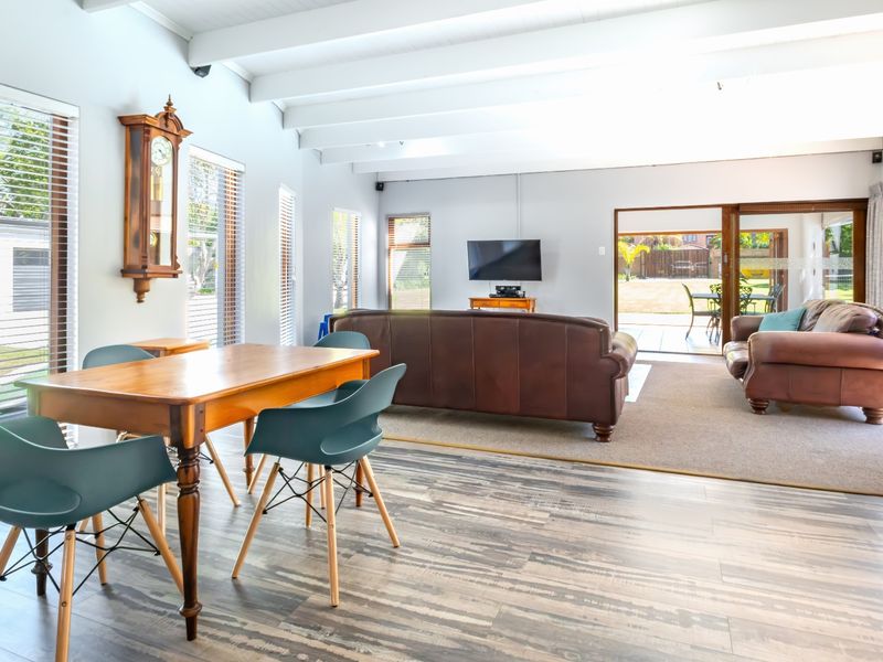 Spacious open-plan living and dining area featuring exposed timber beams, laminate flooring, and large sliding doors providing seamless access to the outdoor patio.