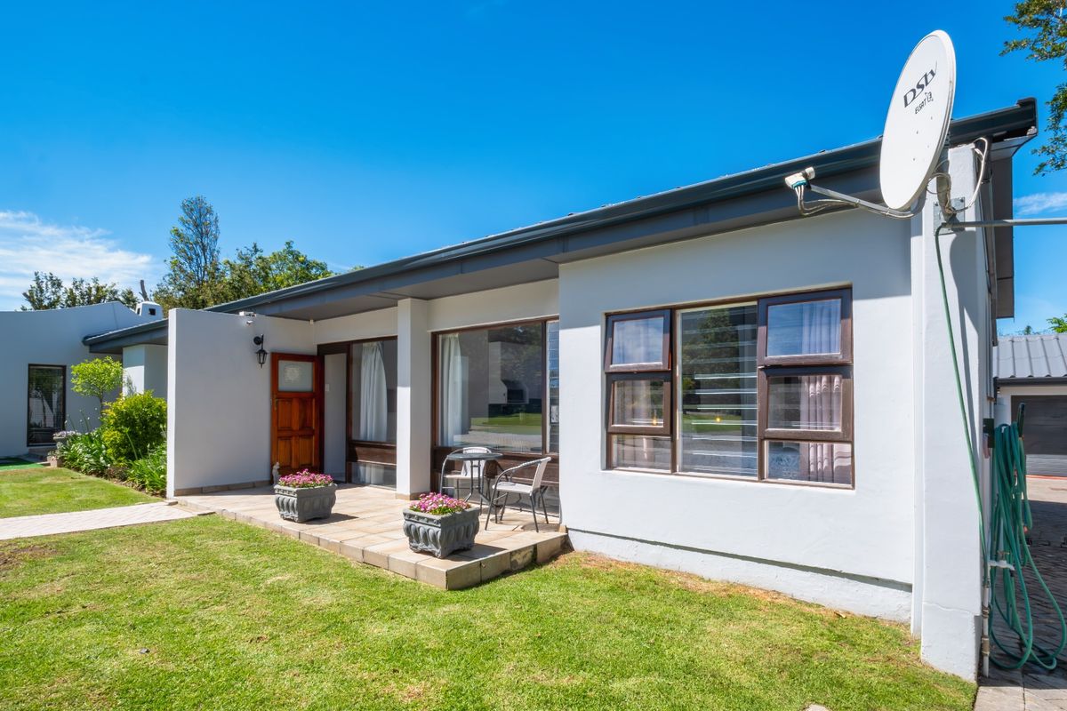 Rear view of the property featuring a tiled patio, well-maintained lawn, and paved driveway access.