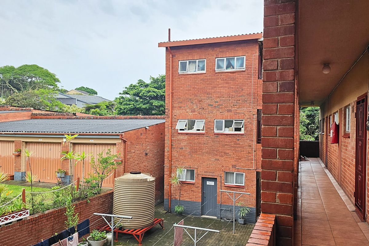 View of the apartment complex rear exterior, featuring a brick facade, paved courtyard area, and communal walkway.