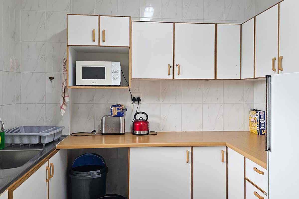 A functional kitchen featuring white cabinetry, laminate countertops, and tiled splashbacks, providing a practical workspace with integrated storage and sink area.