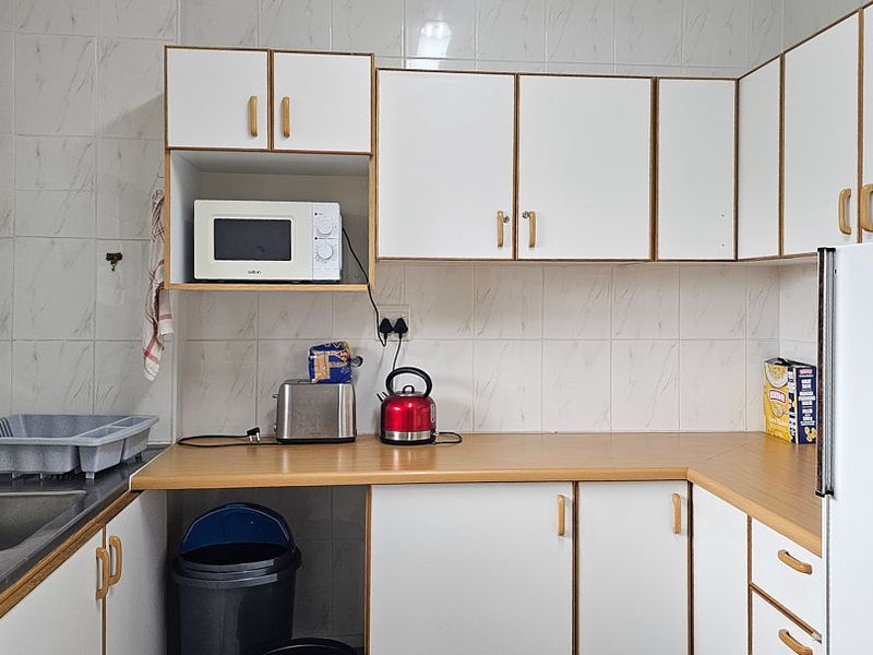 A functional kitchen featuring white cabinetry, laminate countertops, and tiled splashbacks, providing a practical workspace with integrated storage and sink area.