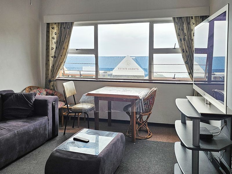 A living room featuring a large window with natural light and carpeted flooring, offering a functional space for relaxation.