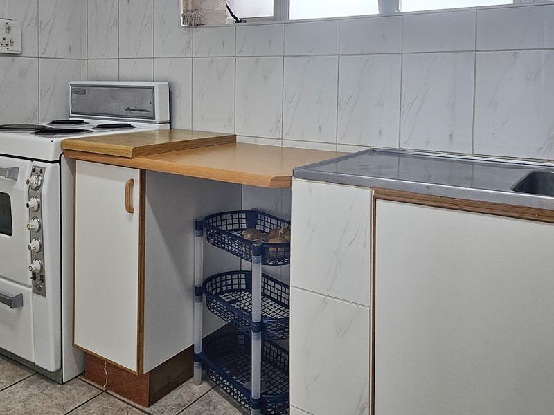 A functional kitchen area featuring a freestanding stove, stainless steel sink, laminate countertops, and tiled wall finishes.