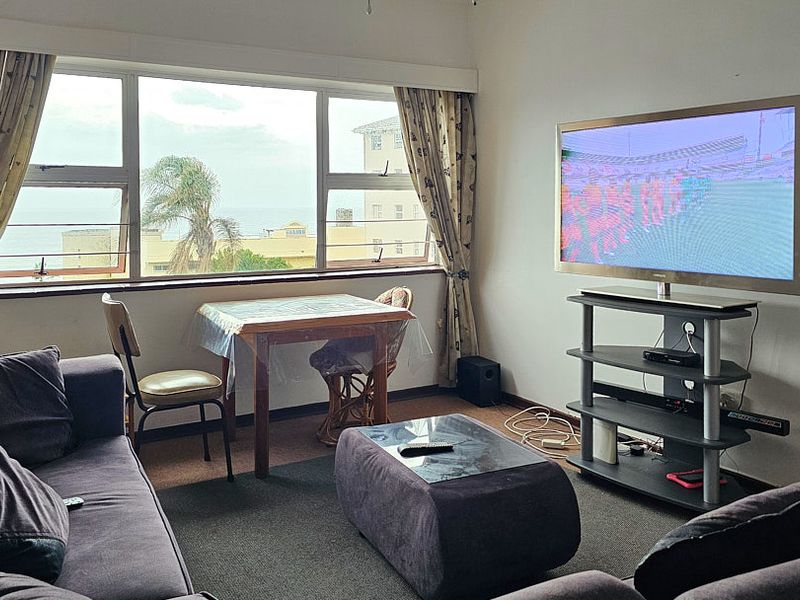 A living room featuring large windows with natural light and views, carpeted flooring, and a functional layout suitable for relaxation.