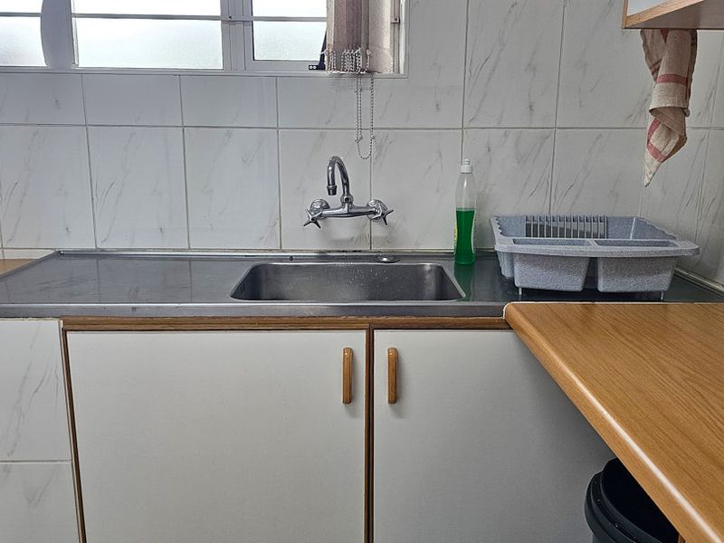 A functional kitchen area featuring a stainless steel sink, laminate countertops, and tiled backsplash with built-in cabinetry.