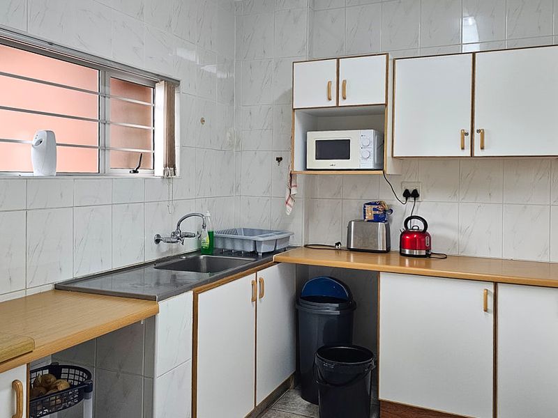 A functional kitchen featuring laminate countertops, white cabinetry, tiled walls, and a stainless steel sink with a window for natural light.