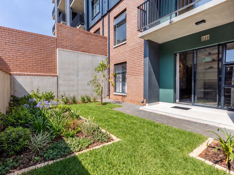 A well-maintained rear garden featuring a paved patio, landscaped lawn, and modern brick and concrete architectural elements with access via sliding glass doors.