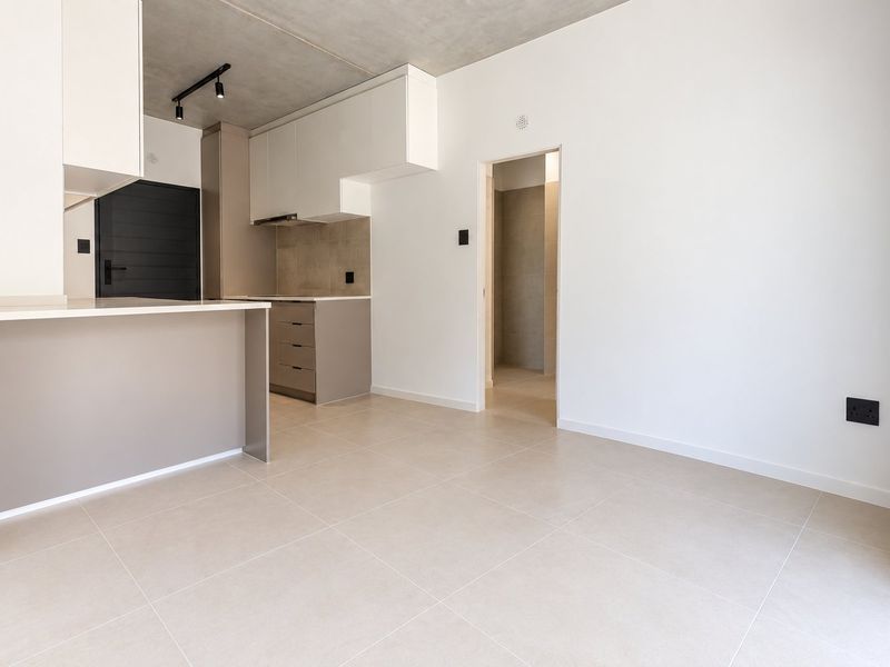 Modern open-plan kitchen and living area featuring sleek built-in cabinetry, stone countertops, exposed concrete ceilings, and neutral tiled flooring.