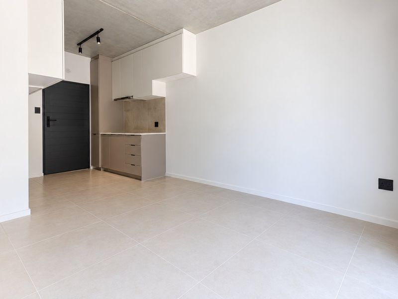 A modern, minimalist open-plan living and kitchen area featuring sleek built-in cabinetry, tiled floors, and an exposed concrete ceiling in excellent condition.