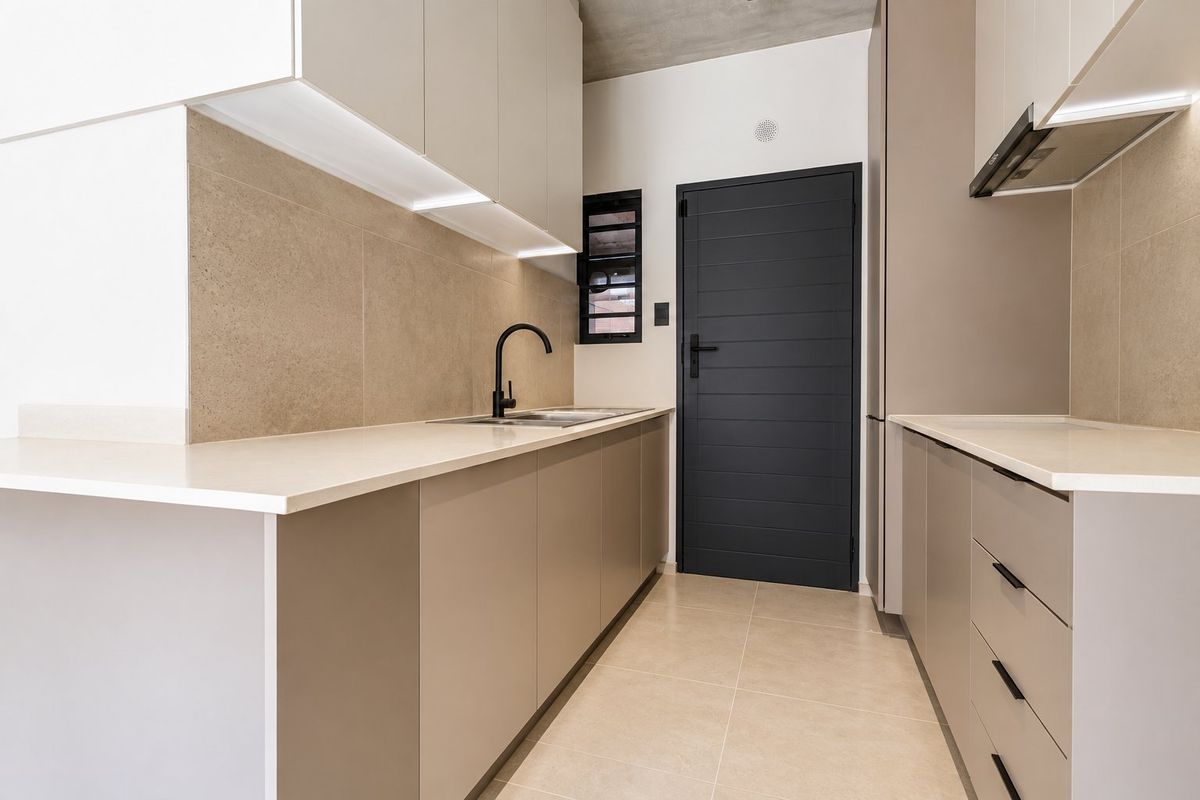 Modern galley kitchen featuring sleek handleless cabinetry, stone countertops, integrated extractor fan, and high-quality tiled finishes with an exposed concrete ceiling.