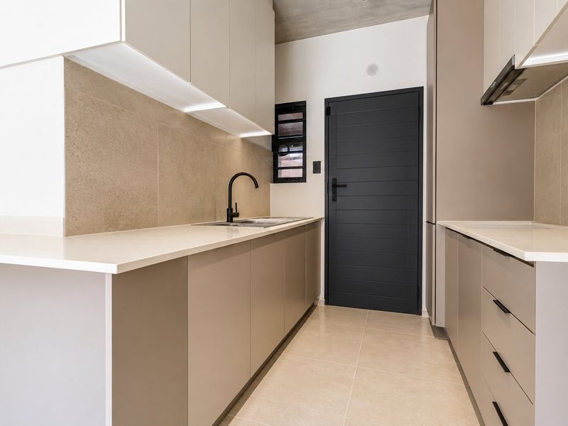 Modern galley kitchen featuring sleek handleless cabinetry, stone countertops, integrated extractor fan, and high-quality tiled finishes with an exposed concrete ceiling.