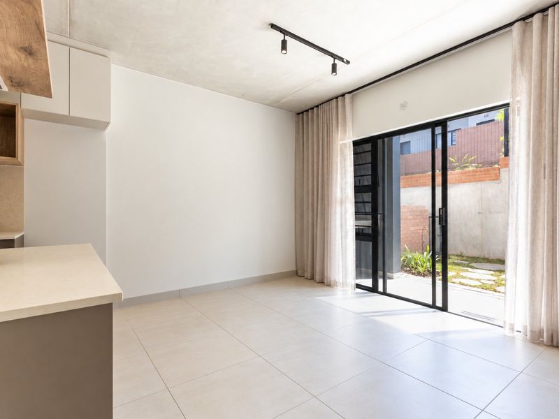 Modern open-plan living area featuring tiled floors, track lighting, and large sliding glass doors opening to a private outdoor space.