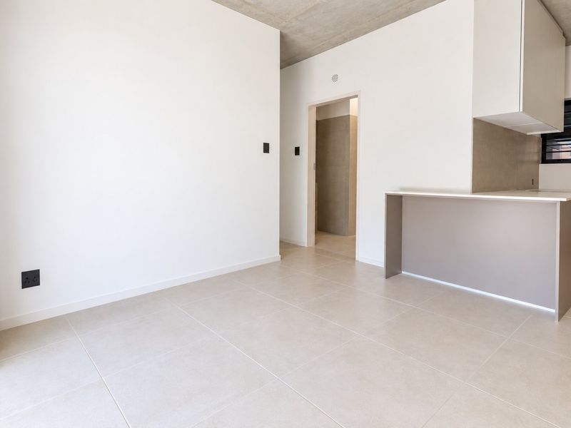 Modern open-plan living area featuring a sleek kitchen with stone countertops, tiled flooring, and an exposed concrete ceiling in a minimalist, vacant space.