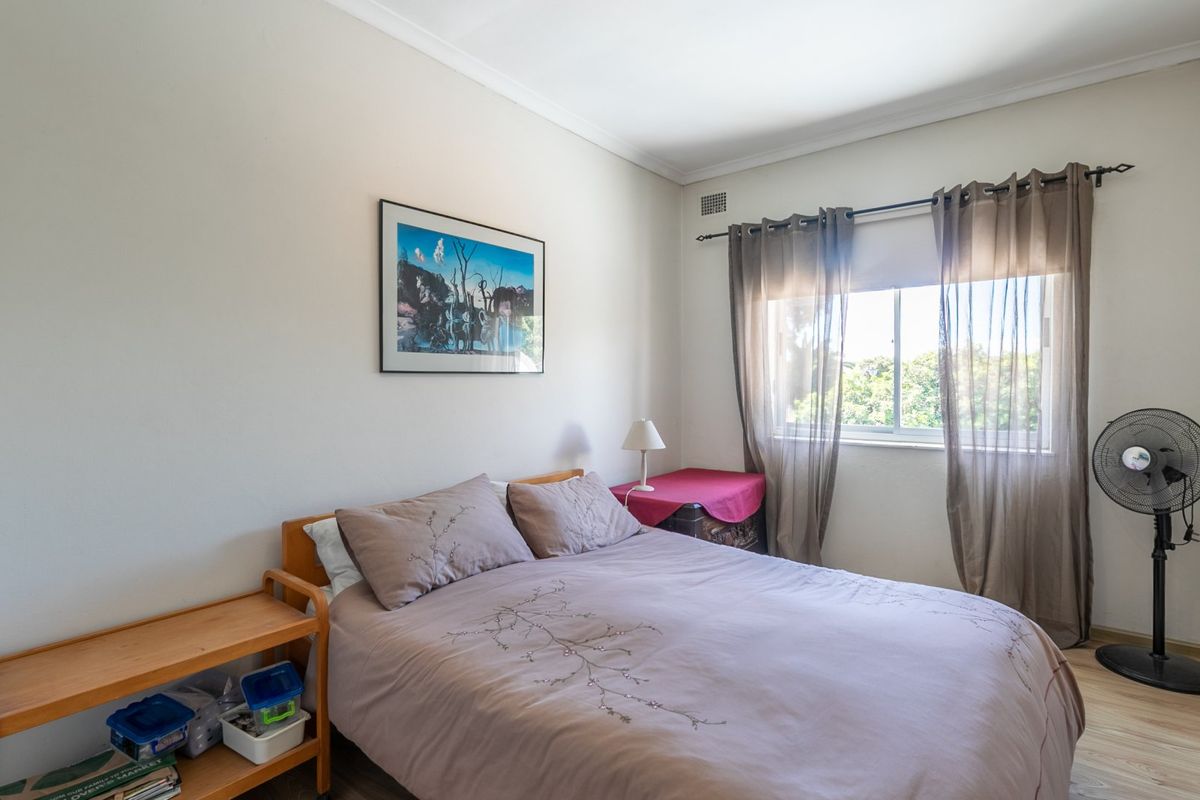 A well-lit bedroom featuring laminate flooring, neutral walls, and a window with natural light, providing a comfortable and functional living space.