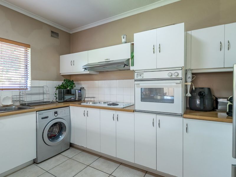 Functional kitchen featuring white cabinetry, laminate countertops, built-in oven, electric hob, and tiled flooring with a neutral backsplash.