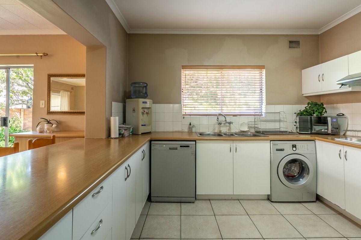 A functional kitchen featuring white cabinetry, laminate countertops, tiled backsplash, and integrated appliance spaces, with direct access to an adjacent living area.