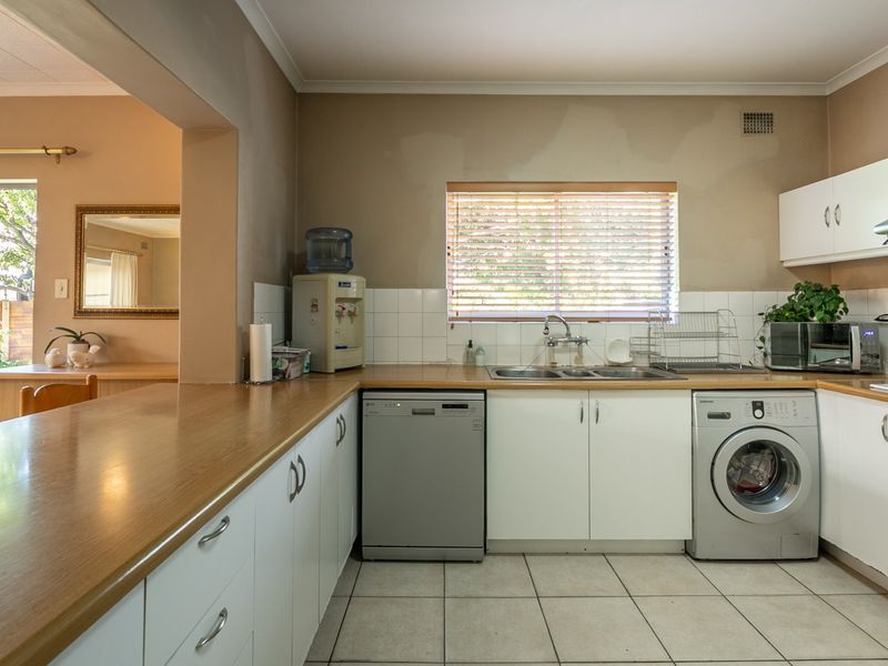 A functional kitchen featuring white cabinetry, laminate countertops, tiled backsplash, and integrated appliance spaces, with direct access to an adjacent living area.