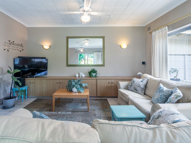 A comfortable living room featuring built-in cabinetry, a ceiling fan, wall sconces, and large sliding glass doors providing natural light.