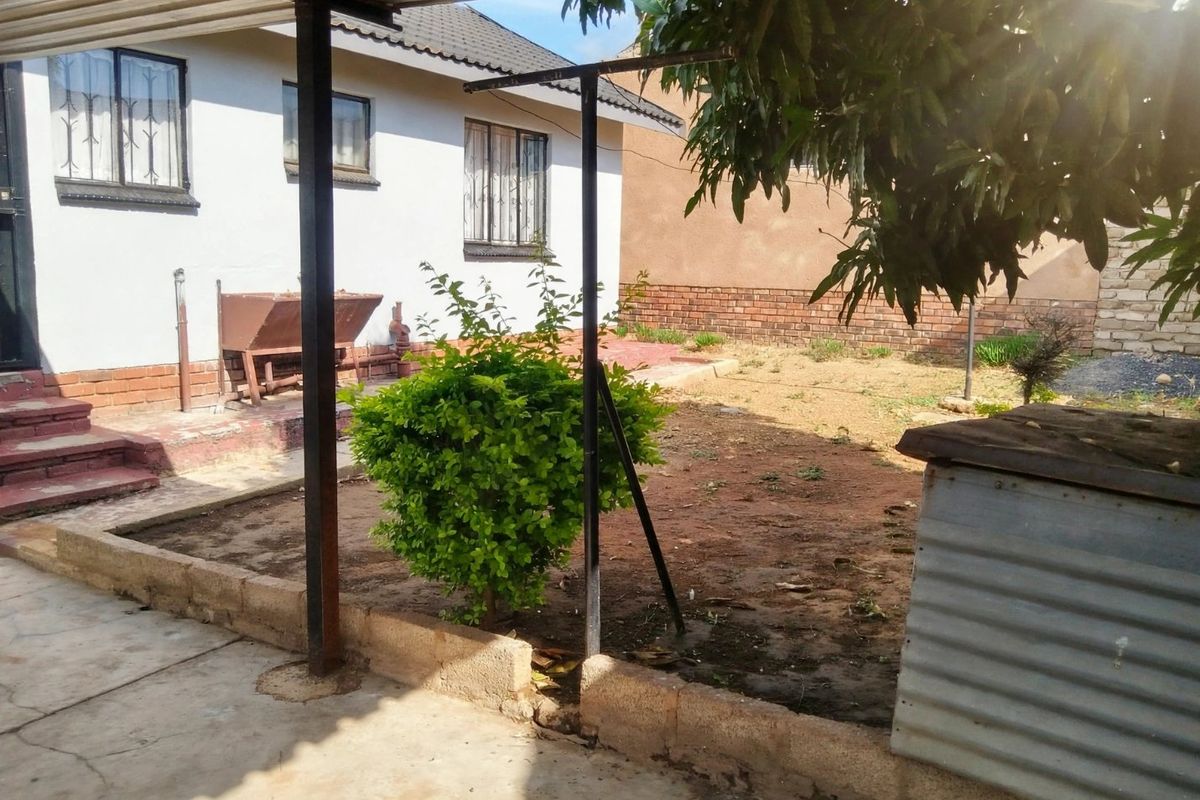 Rear exterior view featuring a concrete patio area, metal roof structure, and a garden space with brick retaining walls.