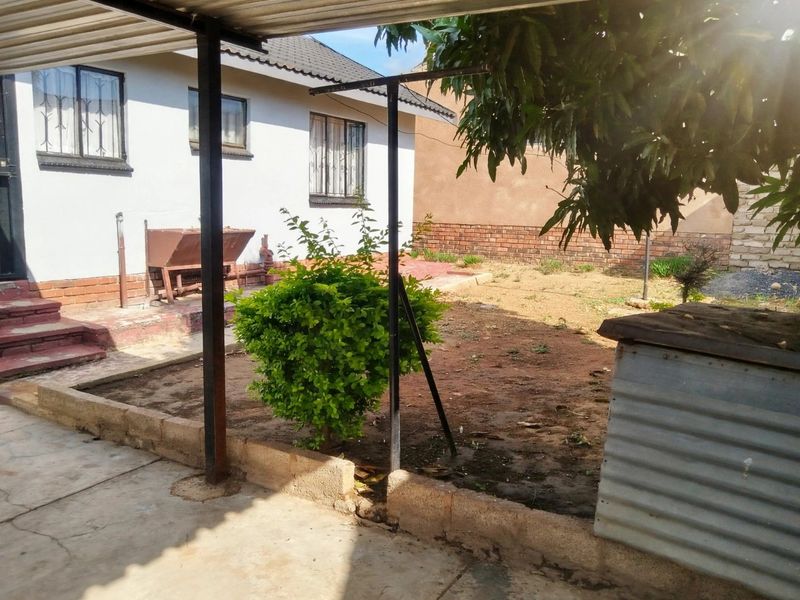 Rear exterior view featuring a concrete patio area, metal roof structure, and a garden space with brick retaining walls.