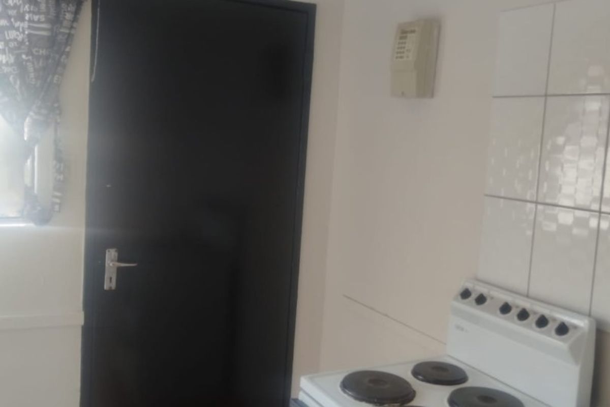 A functional kitchen area featuring a freestanding electric stove, tiled splashback, and tiled flooring.